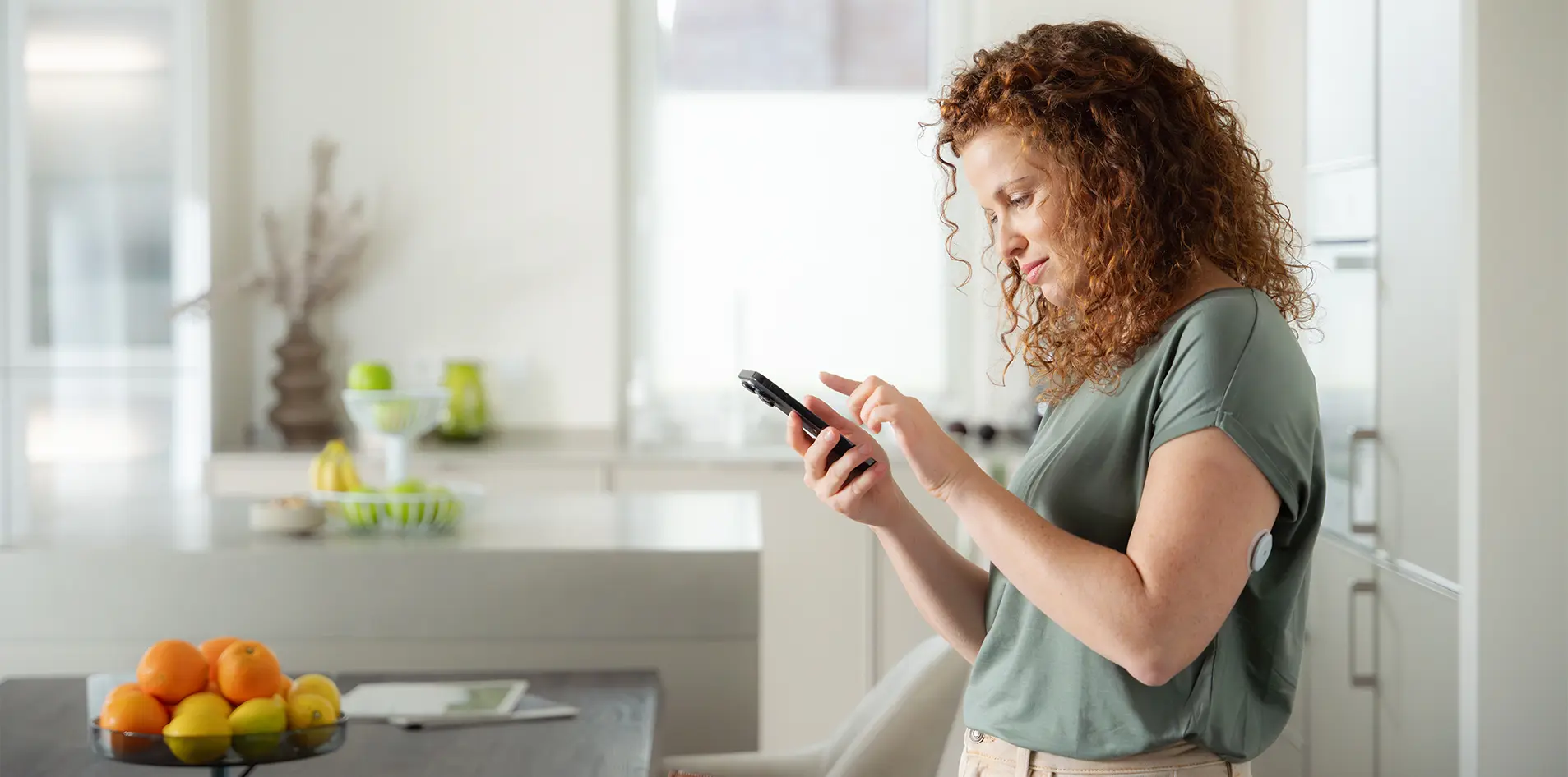 Frau steht in einer Küche und überprüft ihre Zuckerwerte über das Smartphone