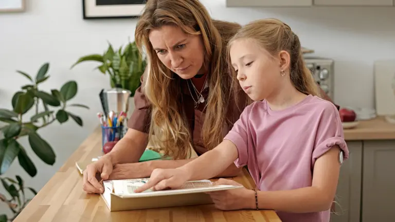 Mutter und Tochter sitzen gemeinsam am Tisch und betrachten ein Buch. Am Oberarm des Mädchens ist ein Glukosesensor zu sehen; die Szene steht für die gemeinsame Bewältigung des Diabetes-Alltags bei etwaigen weiteren Einschränkungen.