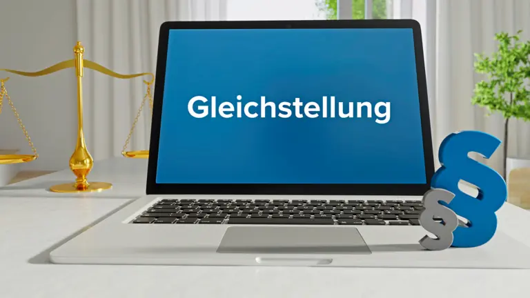 Laptop mit blauem Bildschirm und der Aufschrift „Gleichstellung“; daneben stehen eine goldene Waage und ein Paragraphenzeichen als Symbole für Recht und Gesetz.