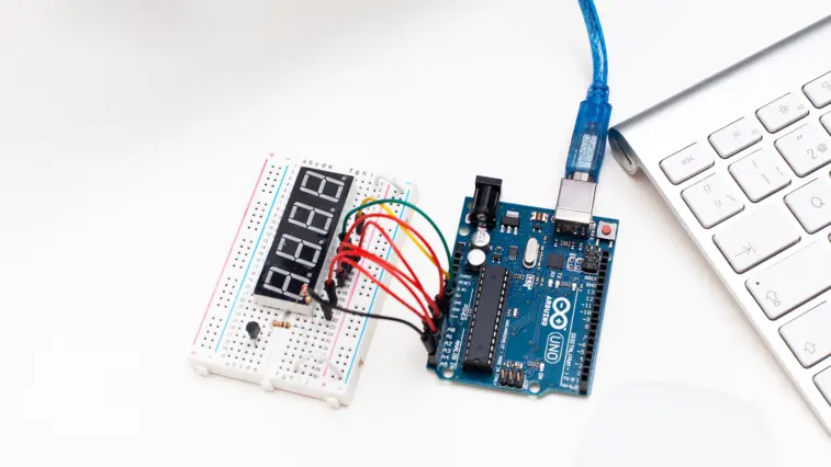 Ein Steckbrett mit Siebensegmentanzeige und farbigen Kabeln ist mit einer Arduino-Platine verbunden, die per USB-Kabel an eine Computertastatur angeschlossen ist. Sinnbild für selbstgebaute Open-Source-Elektronik, wie sie bei DIY-Systemen zur automatisierten Insulindosierung zum Einsatz kommt.