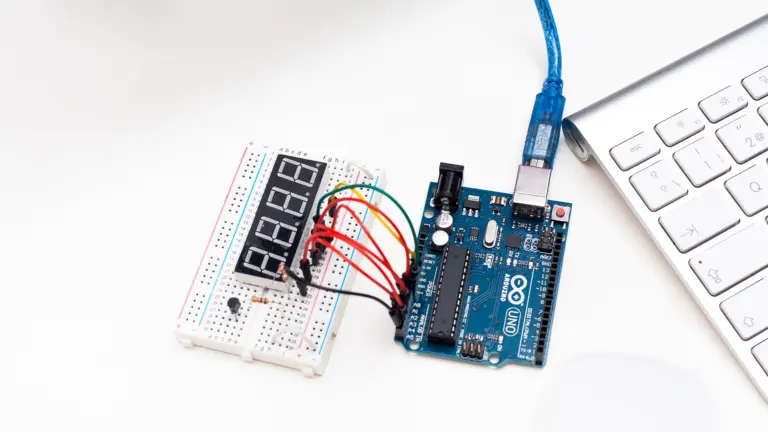 Ein Steckbrett mit Siebensegmentanzeige und farbigen Kabeln ist mit einer Arduino-Platine verbunden, die per USB-Kabel an eine Computertastatur angeschlossen ist. Sinnbild für selbstgebaute Open-Source-Elektronik, wie sie bei DIY-Systemen zur automatisierten Insulindosierung zum Einsatz kommt.