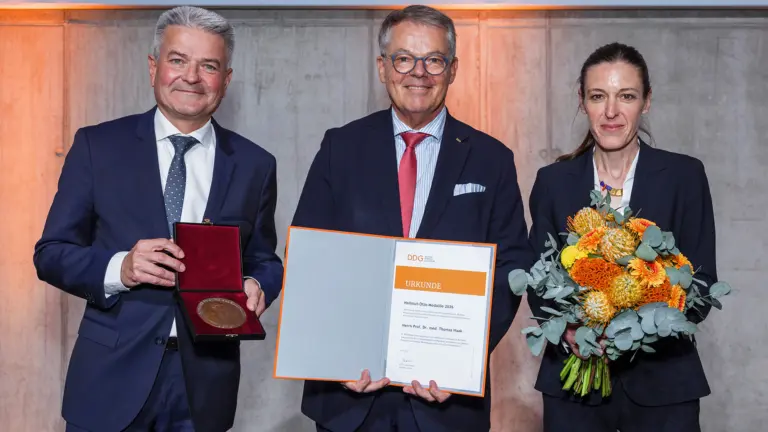 Prof. Dr. Thomas Haak (Mitte) präsentiert gemeinsam mit Prof. Dr. Andreas Seufert (links) und Prof. Dr. Barbara Ludwig seine Urkunde und die Hellmut-Otto-Medaille der Deutschen Diabetes Gesellschaft. Prof. Haak hält zudem die geöffnete Medaillenbox, Prof. Ludwig einen Blumenstrauß.