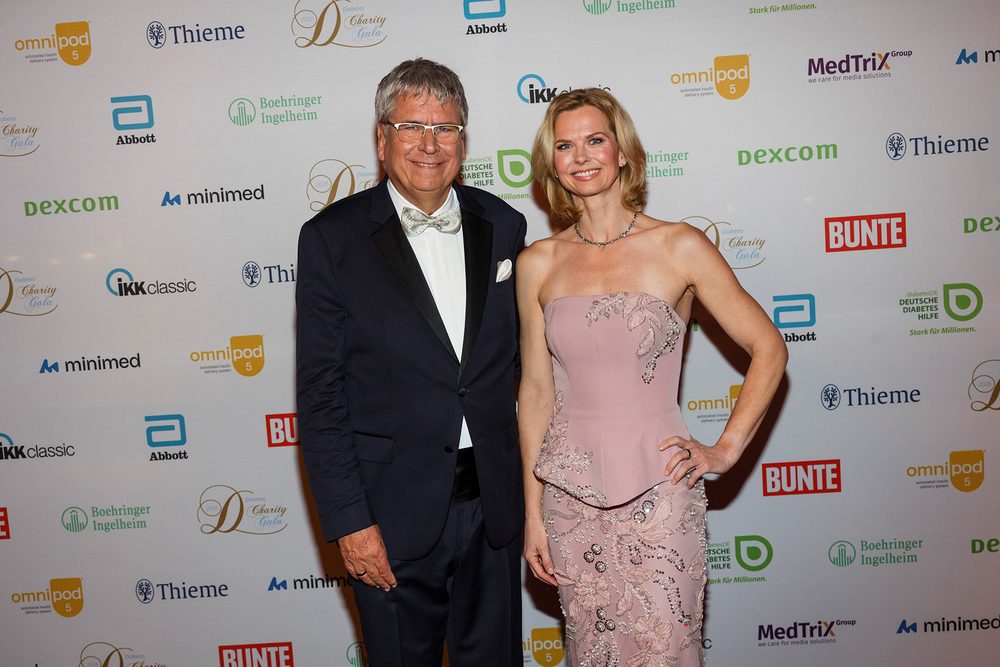 Dr. Jens Kröger im Smoking und Britta Steffen in einem rosafarbenen Abendkleid stehen lächelnd vor einer Fotowand mit Sponsorenlogos.