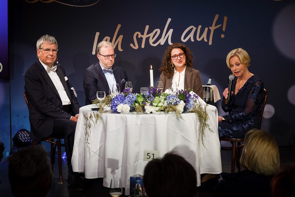 Daniel Lensing und Cornelia Doll sitzen auf der Bühne an einem mit Blumen geschmückten Tisch unter dem Schriftzug „Ich steh auf!“, neben ihnen Dr. Jens Kröger und Nicole Mattig-Fabian mit Mikrofon.