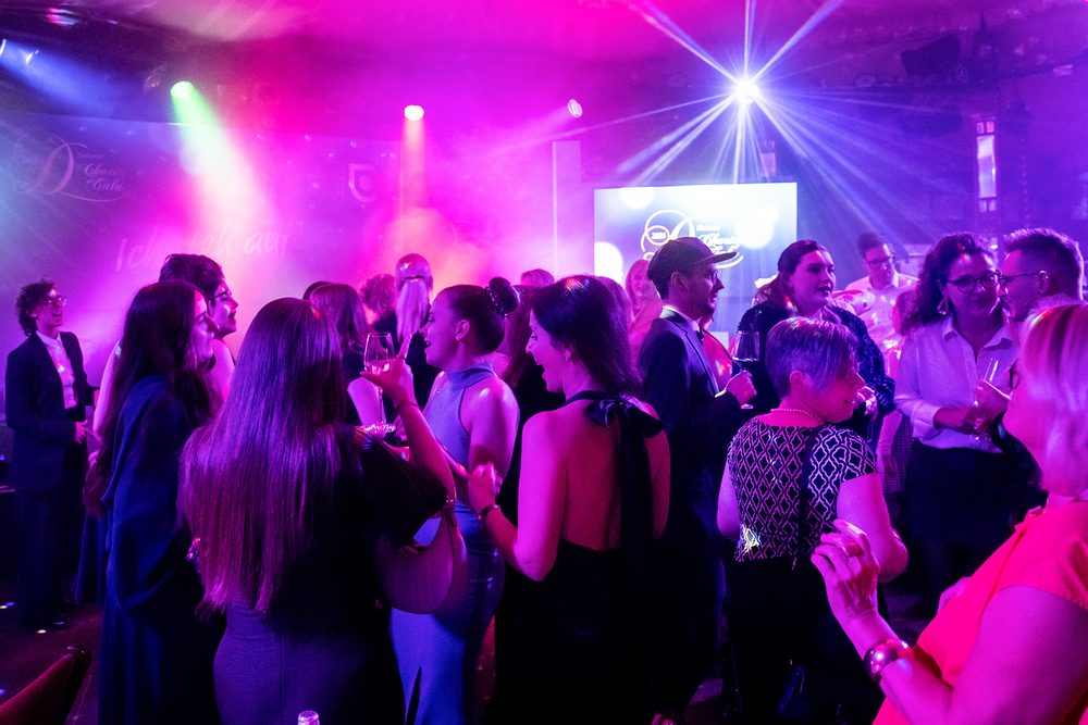 Gäste tanzen dicht gedrängt auf der Tanzfläche der Diabetes-Charity-Gala. Violettes und pinkes Licht beleuchtet den Raum.