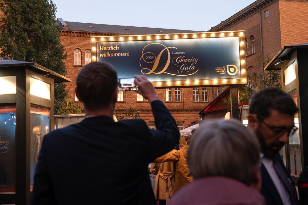 Ein Gast fotografiert das beleuchtete Willkommensschild der Diabetes-Charity-Gala 2026 am Eingang, während weitere Gäste eintreffen.