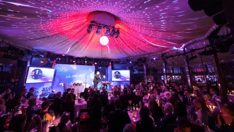 Bei der 15. Diabetes-Charity-Gala in der Berliner „Bar jeder Vernunft“ tritt Georg Stengel auf. Das Publikum sitzt an Tischen vor der violett und pink beleuchteten Bühne.