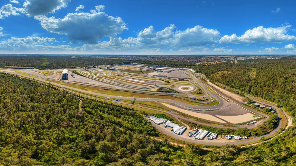 Luftaufnahme der Rennstrecke Hockenheimring mit Kurven, Fahrbahnen und Tribünen, umgeben von Wald und Feldern.