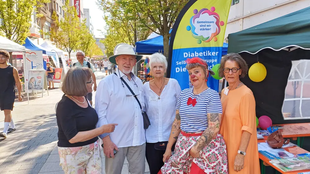 Vier Mitglieder der Diabetiker-Selbsthilfegruppe und eine Clownin stehen vor dem Infostand in der Offenbacher Fußgängerzone. Hinter ihnen ist ein Banner mit der Aufschrift „Gemeinsam sind wir stärker!“ zu sehen.