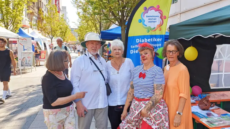 Vier Mitglieder der Diabetiker-Selbsthilfegruppe und eine Clownin stehen vor dem Infostand in der Offenbacher Fußgängerzone. Hinter ihnen ist ein Banner mit der Aufschrift „Gemeinsam sind wir stärker!“ zu sehen.