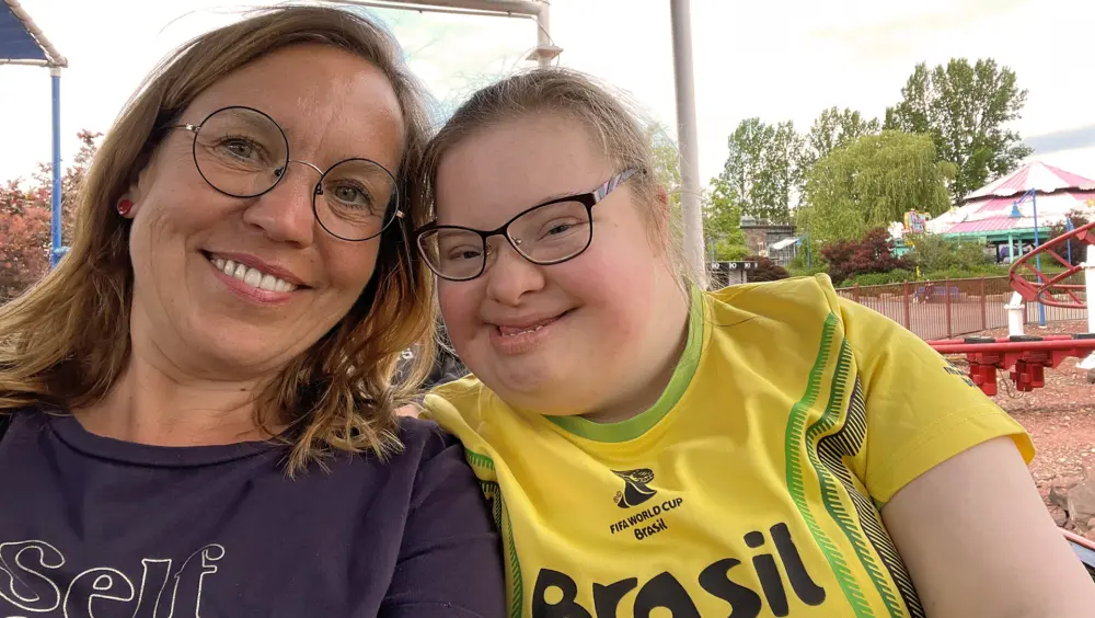 Selfie von Diabetesberaterin Doreen Haberkorn und einem lächelnden Mädchen in einem gelben Brasilien-Trikot auf einem Jahrmarkt, im Hintergrund Fahrgeschäfte und Bäume.