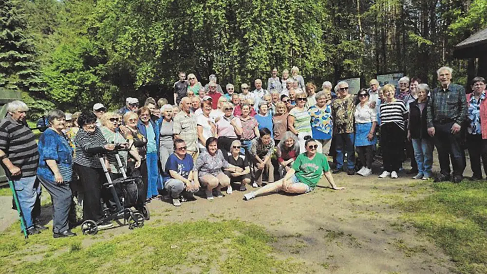 Gruppenfoto von Teilnehmenden des deutsch-polnischen Treffens vor einem Wald. Einige sitzen oder knien in der ersten Reihe, andere stehen dahinter; links sind Gehstöcke und ein Rollator zu sehen.