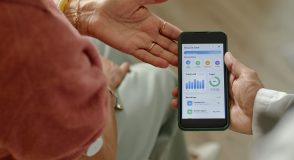 Eine Person mit Glukosesensor am Oberarm betrachtet gemeinsam mit einer zweiten Person die Diabetesdaten auf einem Smartphone. Die Anzeige zeigt Blutzuckerwerte, Tagesverlauf und dokumentierte Mahlzeiten.