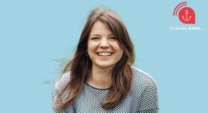 Porträt der lachenden Psychologin Laura Klinker vor hellblauem Hintergrund, mit langen braunen Haaren und gemustertem Pullover; oben rechts das Logo des Diabetes-Anker-Podcasts.